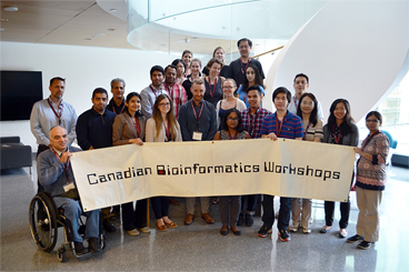 An image of approximately 20 people standing in the OICR lobby holding the Canadian Bioinformatics Workshops banner.